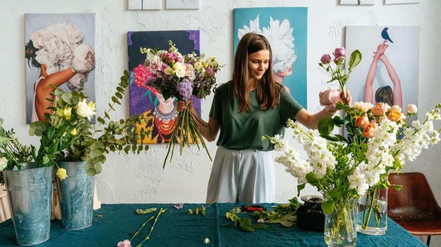 Startseite des Musterladens Blumen Morgentau: Floristin bindet einen Strauß in der Werkstatt